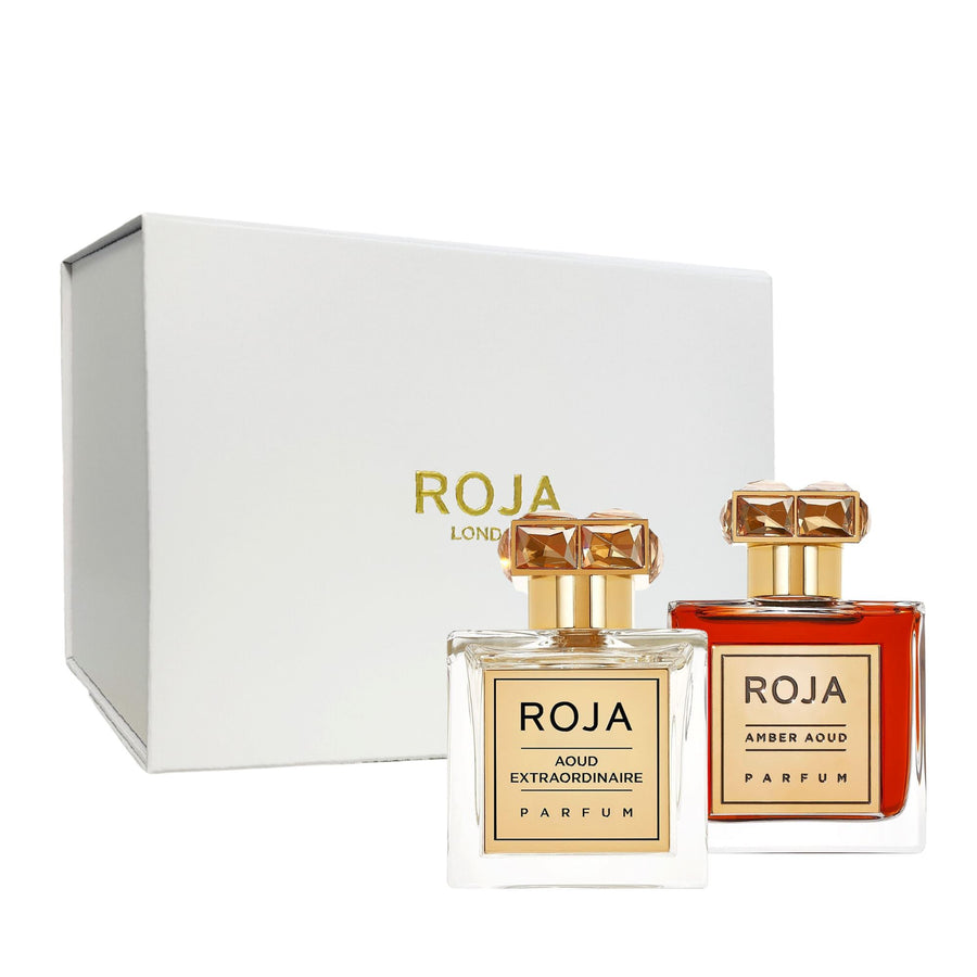 Two elegant bottles from Roja Parfums The Aoud Layering Gift Set, topped with gold caps and featuring rectangular labels, stand before a white box adorned with Roja London in luxurious gold lettering.